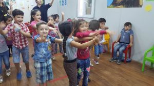 [Image description: Several smiling children with their arms outstretched waving to someone off camera.]