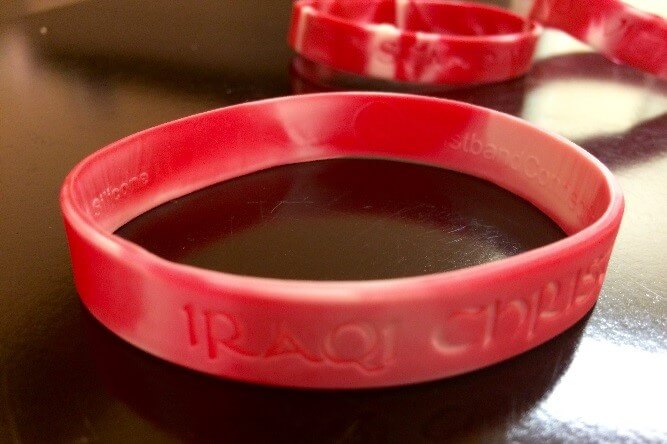 [Image description: photograph of a red marbled plastic wristband on a table. The words "IRAQI CHRISTIANS" can be seen on the outside of the wristband.]